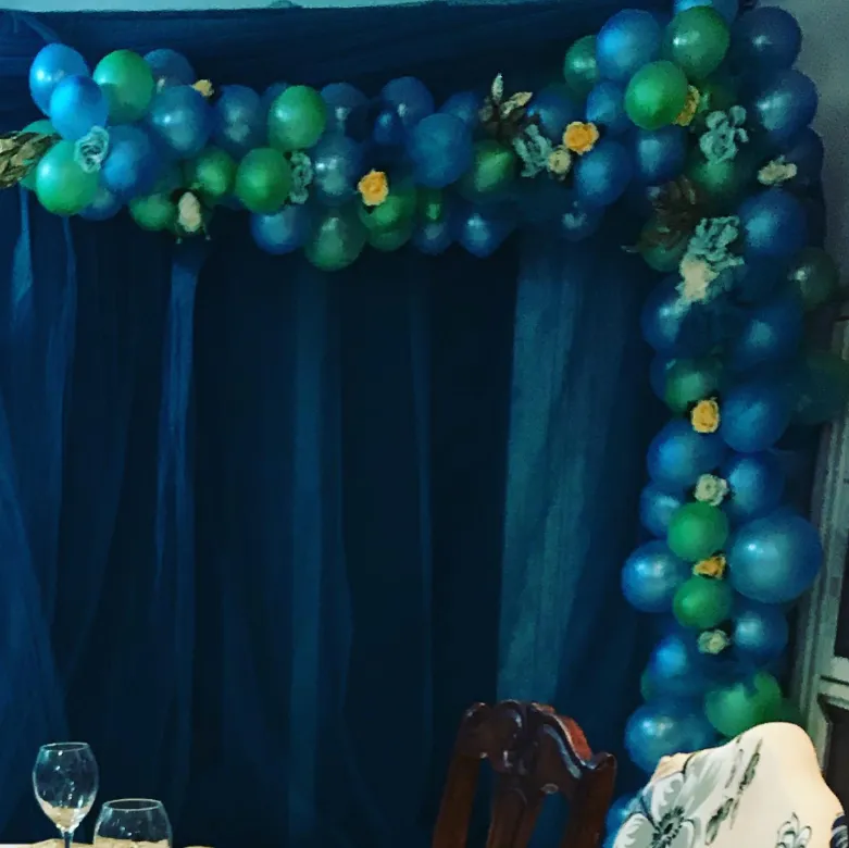 Blue and green organic balloon garland with yellow and white roses framing a draped backdrop