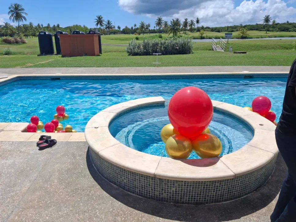 Red and gold balloon clusters at a poolside celebration in Tobago